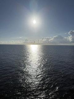 Sun setting over ocean horizon with light reflecting on water and scattered clouds in blue sky