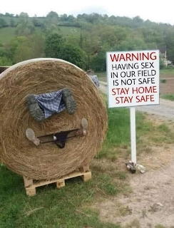 Round hay bale on pallet next to a warning sign about staying home and staying safe during COVID-19