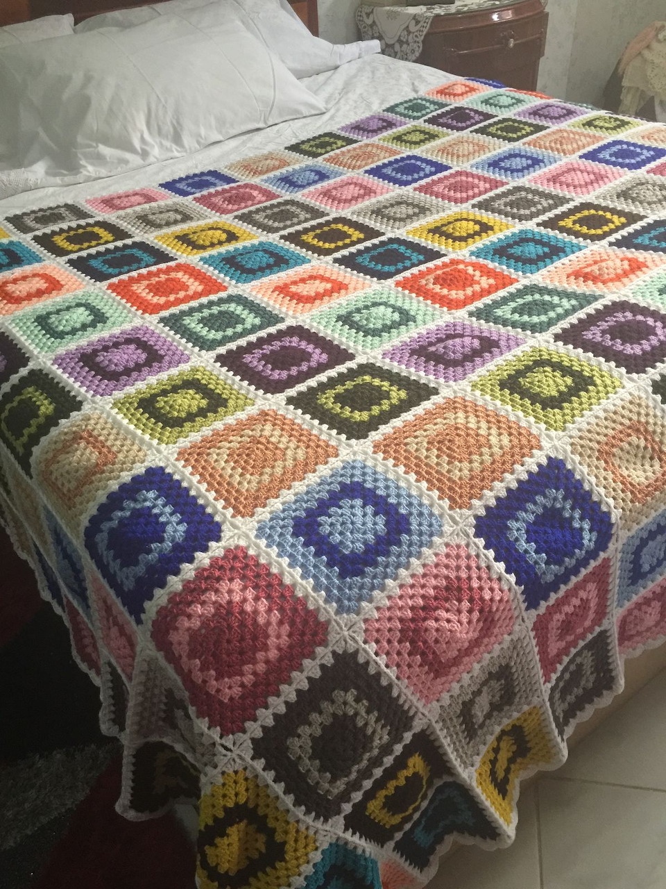 Bed with a colorful crocheted granny square blanket in a bedroom