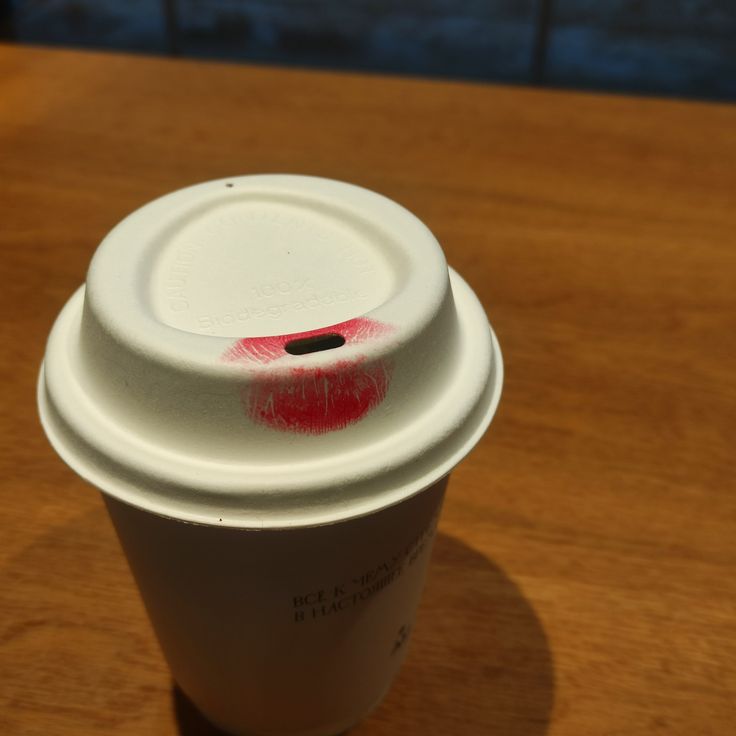 Disposable coffee cup with white lid and red lipstick stain on a wooden table