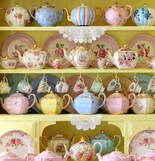 Shelves displaying colorful vintage teapots and teacups with floral patterns and lace doilies
