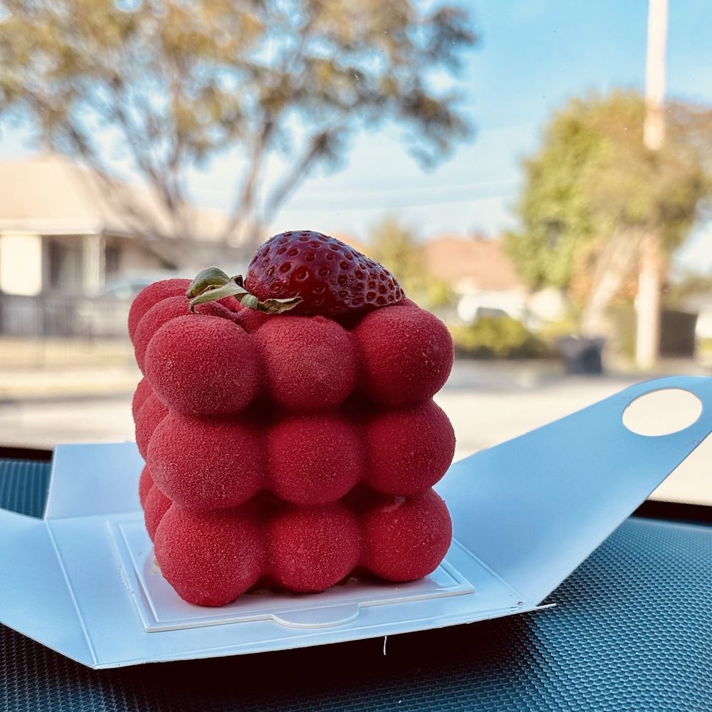 Strawberry-shaped red dessert on a white tray with a blurred outdoor background