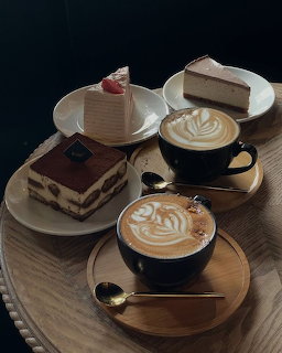 Two lattes with latte art alongside tiramisu and layered cake slices on a wooden café table