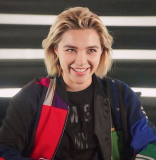 Smiling blonde woman in colorful jacket and black graphic tee against striped wall