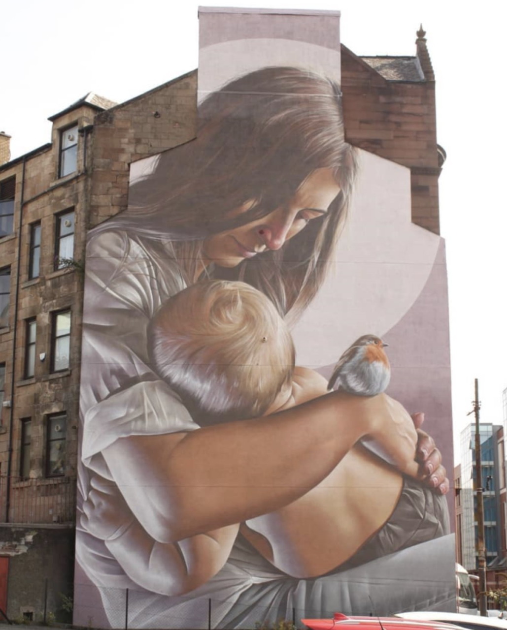 Large mural of a woman hugging a child painted on the side of a brick building