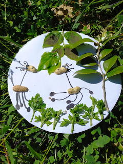 White plate with peanut shell bug crafts made with wire legs, placed among green garden plants