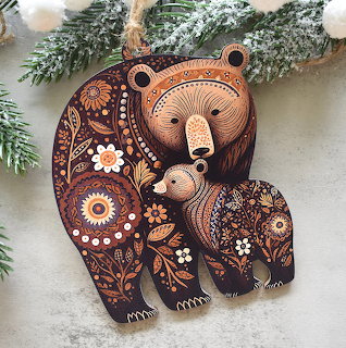 Folk art wooden bear ornament with detailed floral patterns and small bear cub, nestled among snowy pine branches