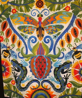 Colorful folk art quilt with central butterfly motif surrounded by flowers, birds, and salamanders in symmetrical design