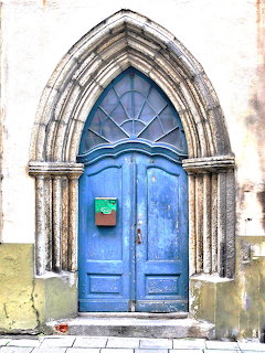 Blue medieval door with carved Gothic stone arch on weathered white wall