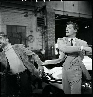 Two men fighting near a car in a black-and-white vintage urban scene