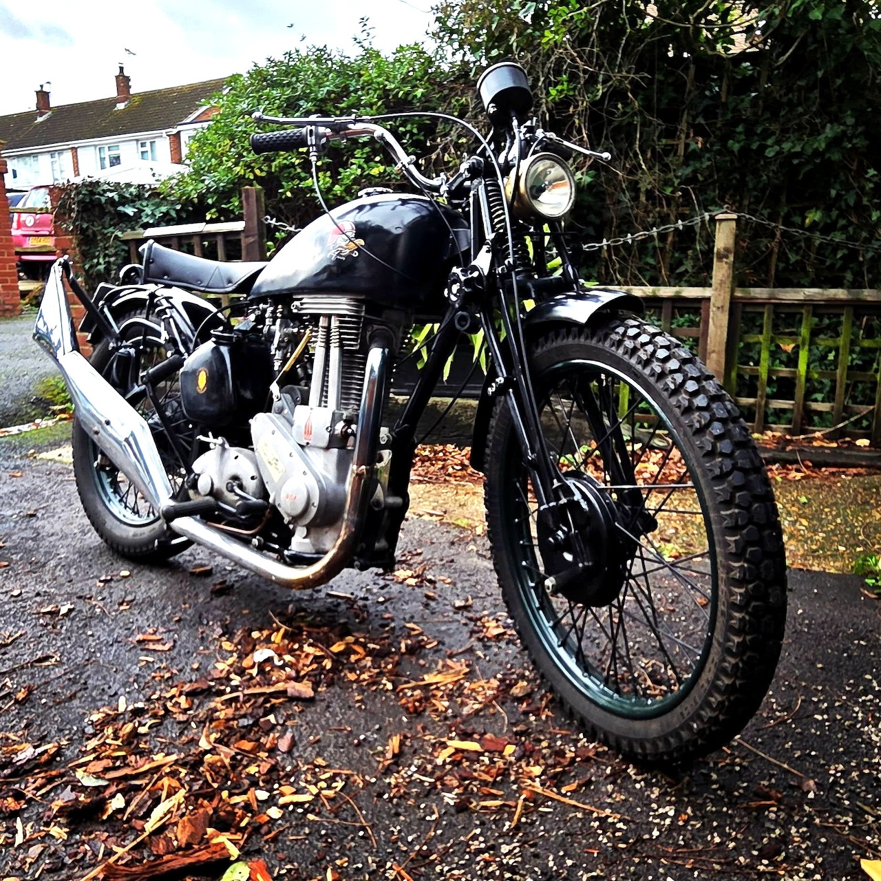 Vintage 1952 BSA M21 motorcycle on gravel with residential houses in background
