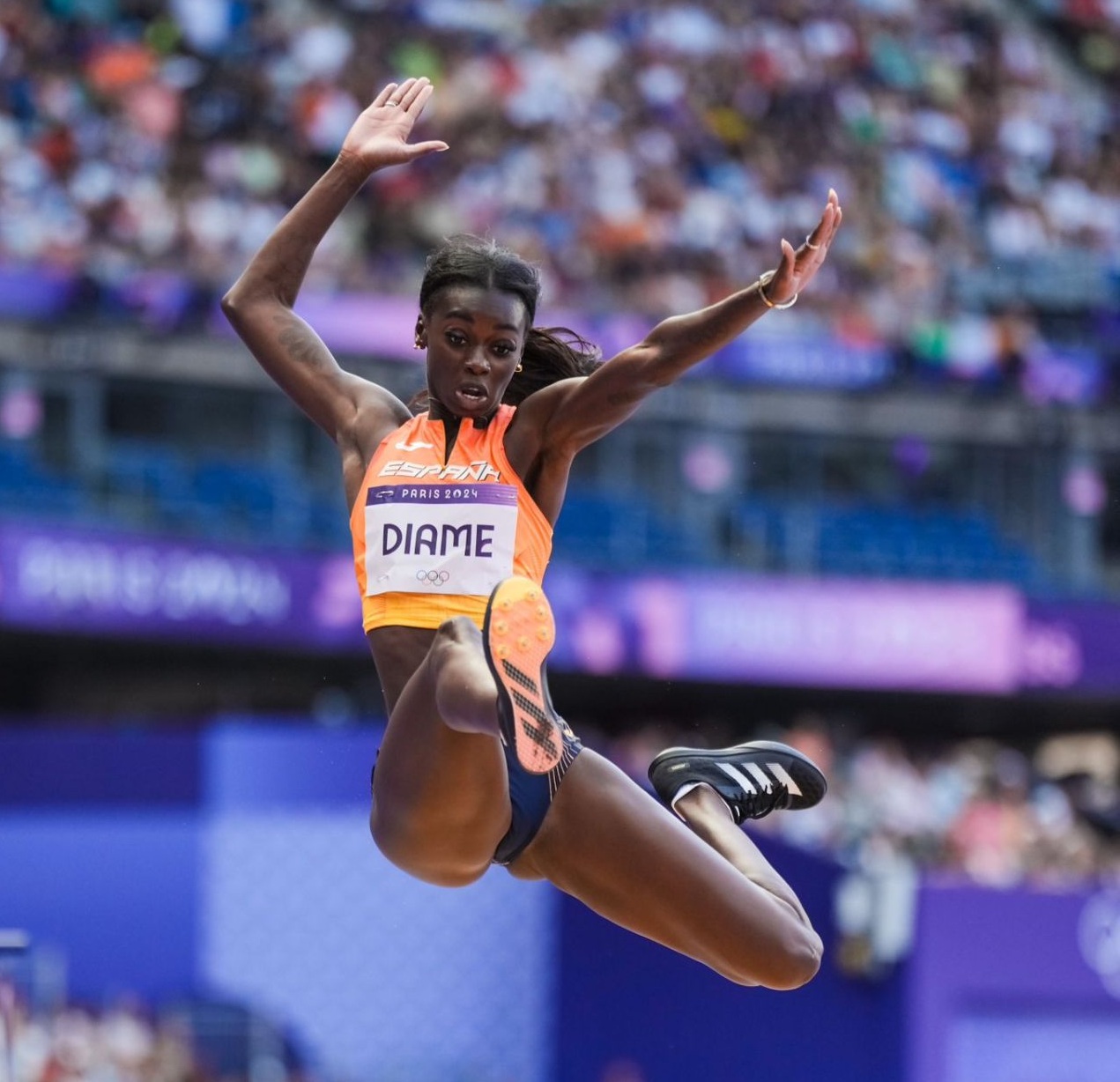 Female athlete mid-air during long jump competition in stadium