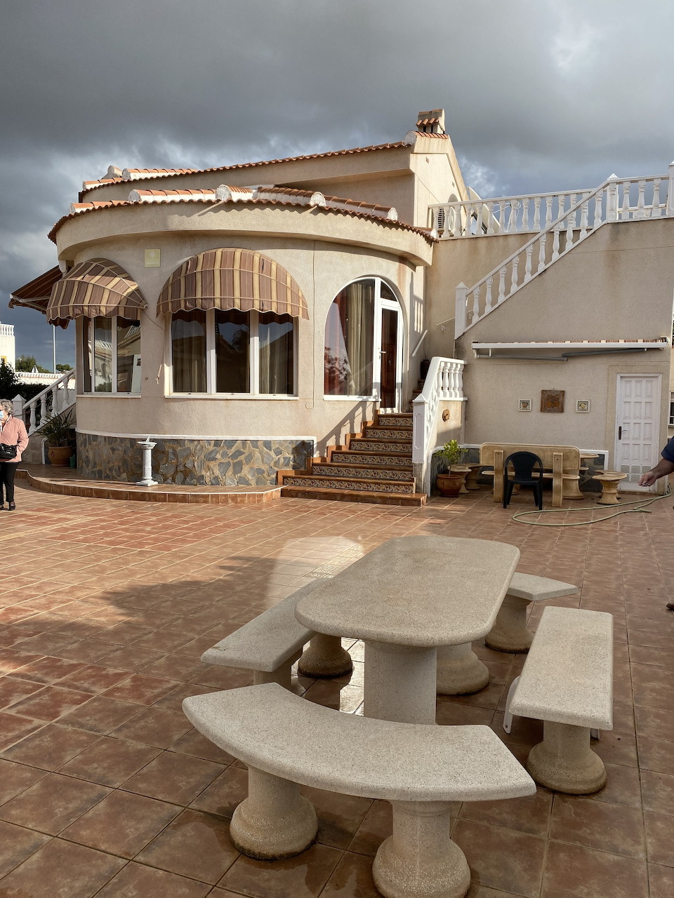 Stone picnic table on a terrace in front of a Mediterranean-style villa with arched windows