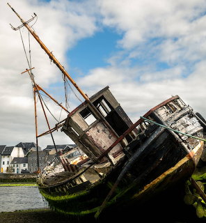 Two old abandoned fishing boats resting on shore at Galway port with houses in the background