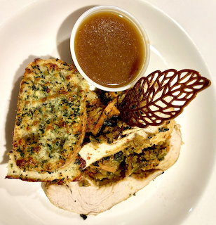 White plate with sliced stuffed chicken, gravy in a small bowl, and a decorative crisp garnish