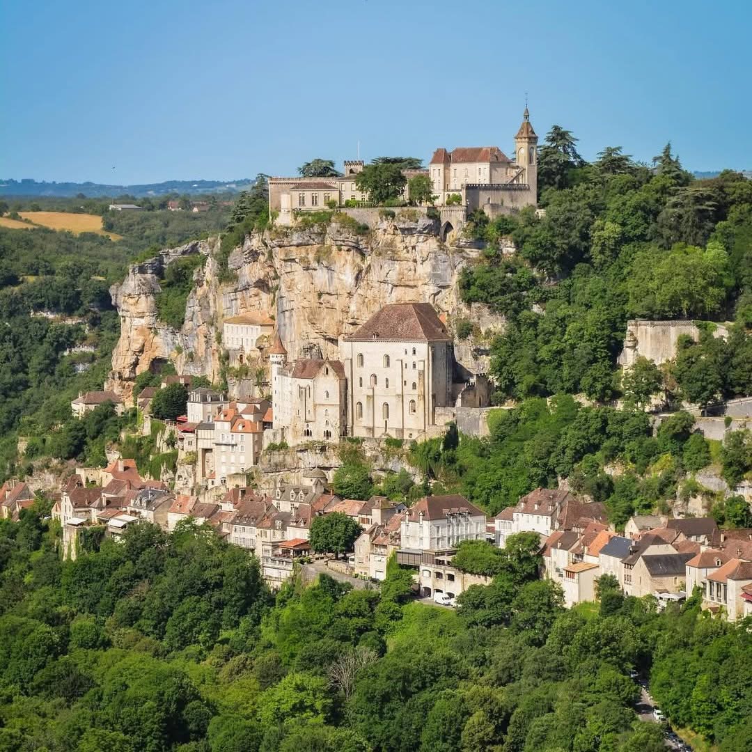 Cliffside village with stone houses and a church built into a rocky hillside above green trees