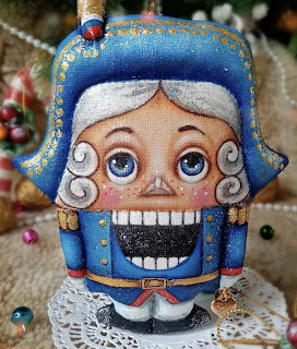 Handmade blue nutcracker fabric ornament with painted face and white hair on lace doily
