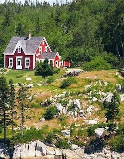 Red house with white trim on a rocky hillside surrounded by green trees and forest