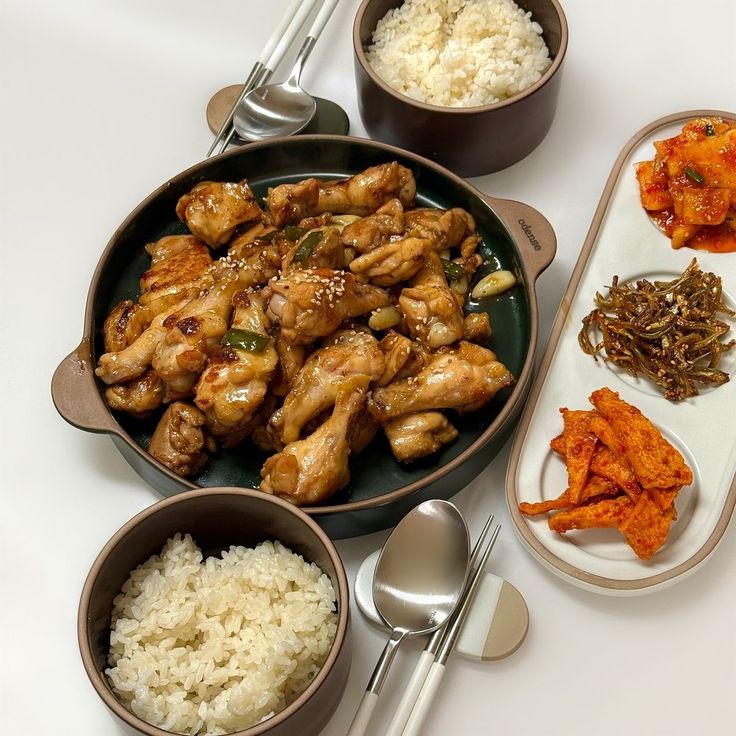 Korean meal with glazed chicken, rice bowls, kimchi and side dishes on a white table
