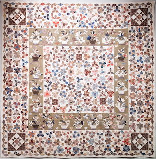 Square folk art quilt with basket appliqués and patchwork border in earth tones