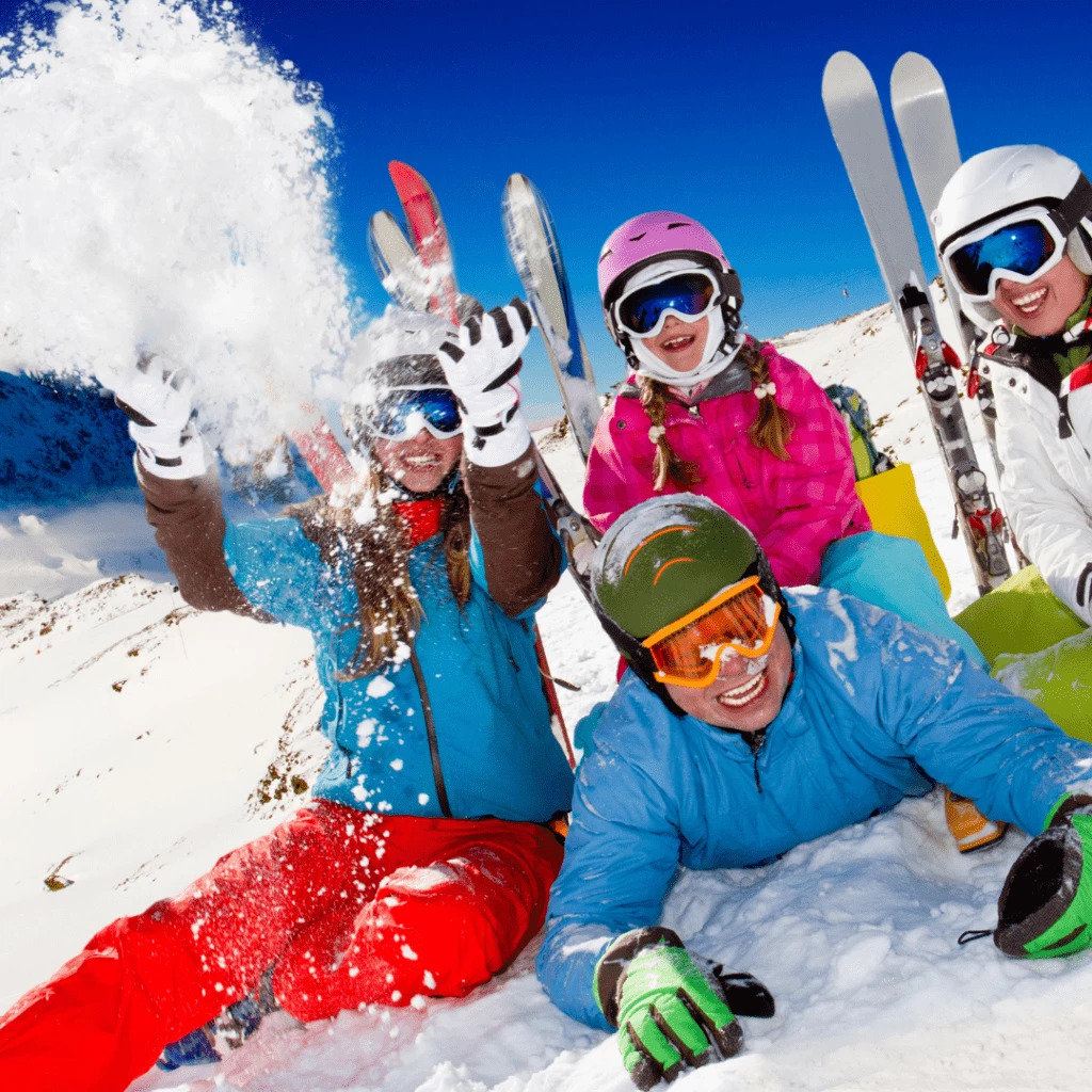 Four happy skiers in colorful jackets playing in the snow on a sunny mountain slope