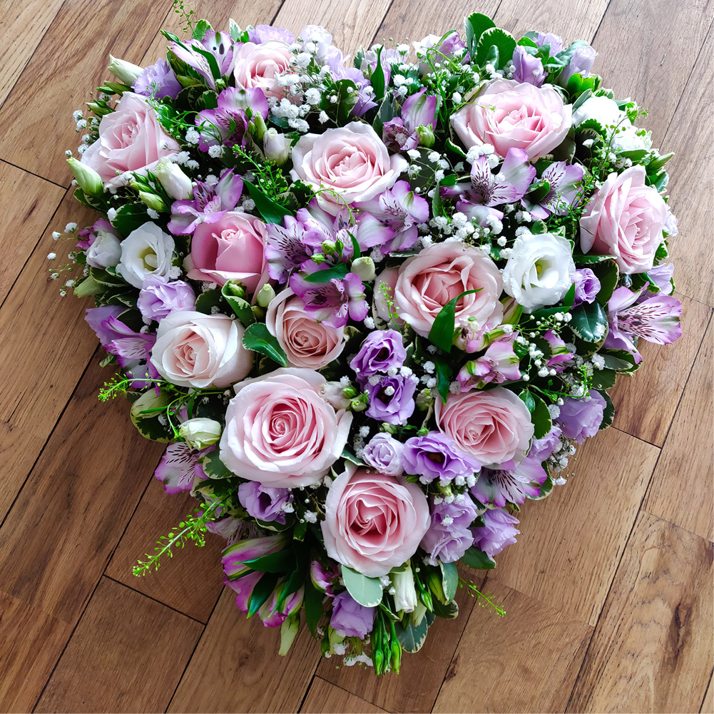 Heart-shaped arrangement of pink roses, purple and white flowers with greenery on wood floor