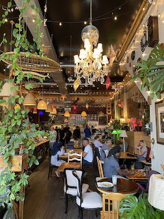 Lush plant-decorated café interior with diners, string lights, and a crystal chandelier