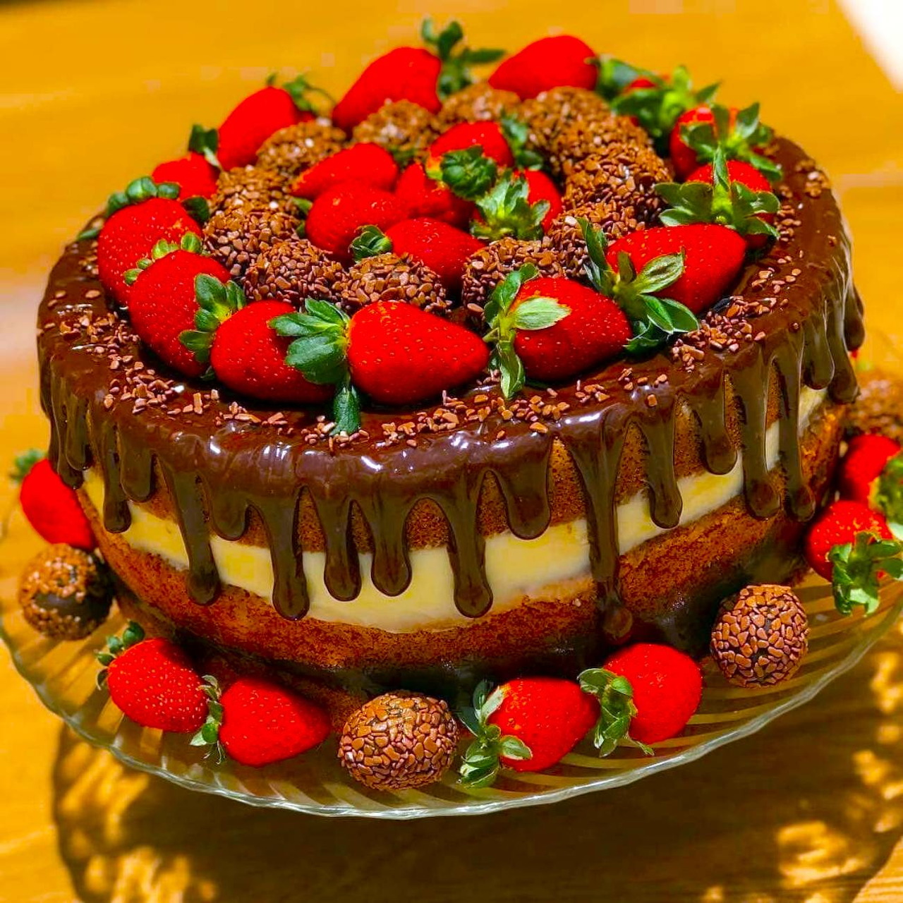 Chocolate layer cake decorated with strawberries and chocolate truffles, drizzled with ganache