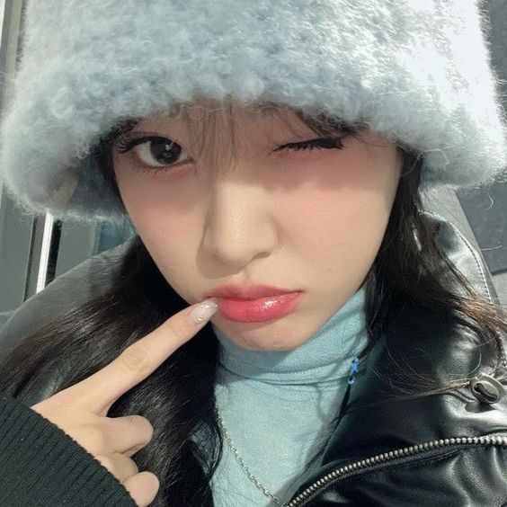 Close-up selfie of a winking young woman wearing a fluffy hat and black jacket