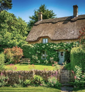 Thatched cottage with ivy walls, garden flowers, wooden gate and bench in sunny yard