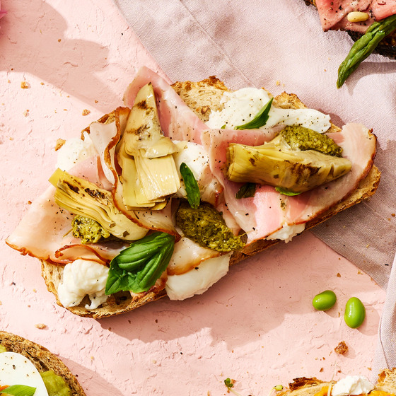 Open sandwich with porchetta, mozzarella, and grilled artichoke on bread with pink background