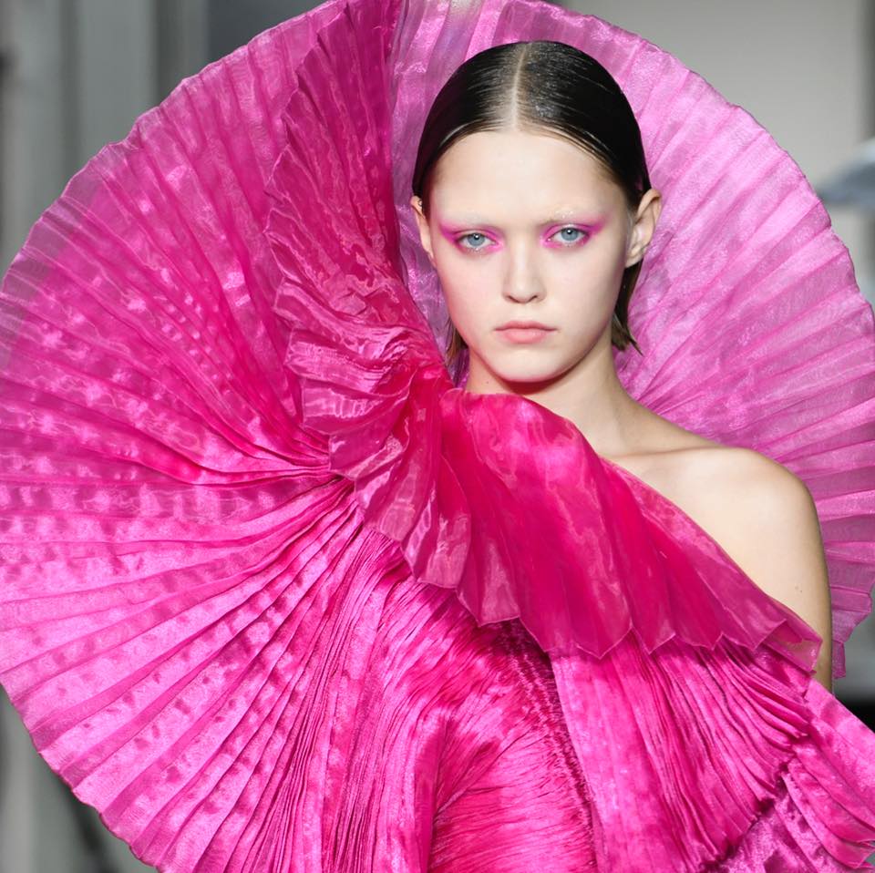 Model wearing oversized pink pleated couture gown with dramatic ruffled fan collar on runway