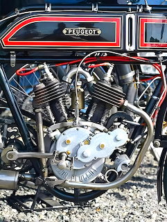 Vintage Peugeot v-twin motorcycle engine with chrome pipes and brass fittings on a black frame