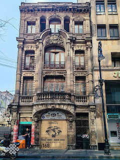 Ornate historic stone building facade on a city street with arched windows and a closed storefront