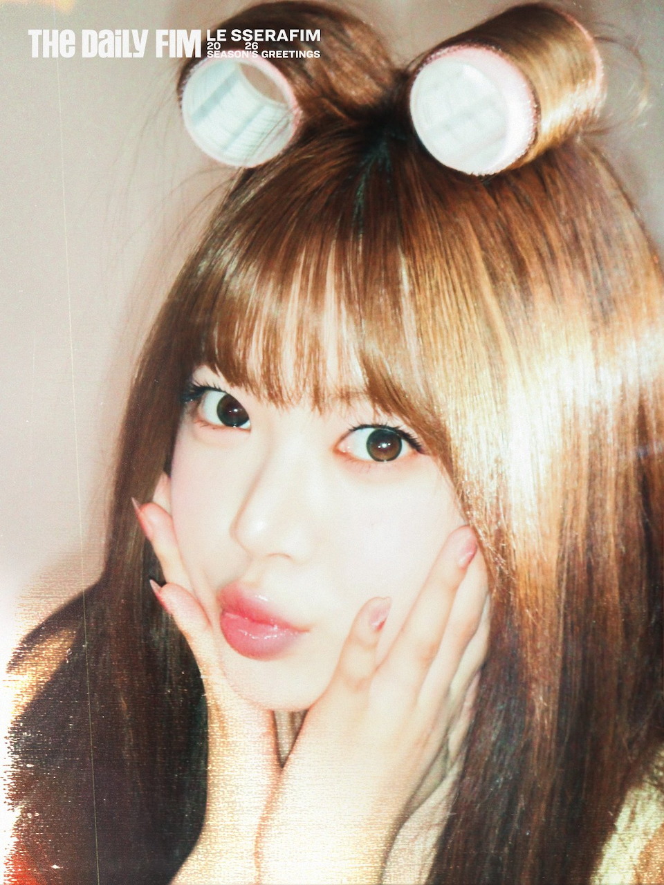 Close-up of young woman with hair rollers and bangs, hands touching her face, warm tones