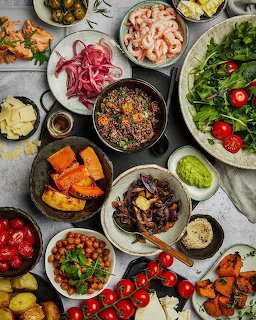 Overhead flat lay of colorful meal with salmon, salads, shrimp, vegetables and side dishes on white background
