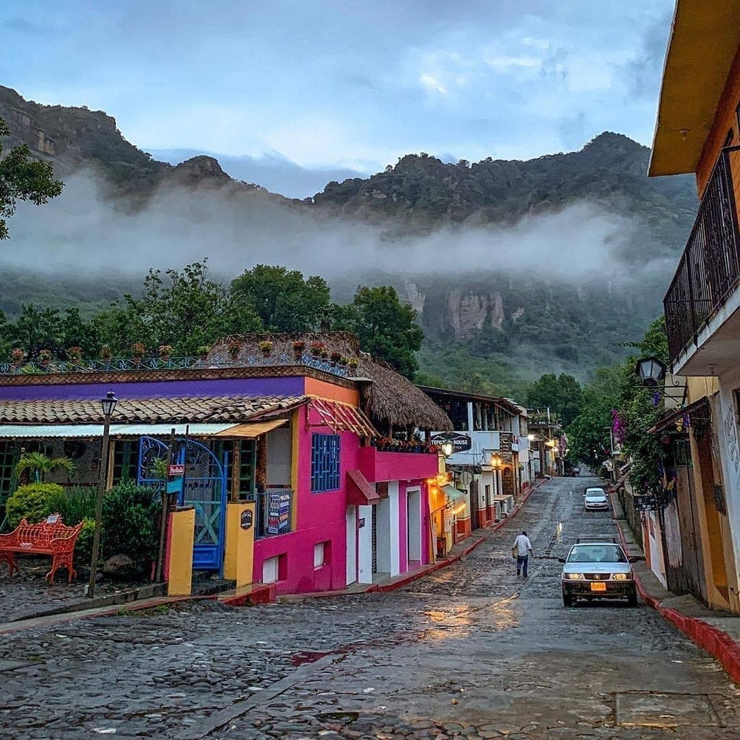 Colorful street in Tepoztlán, Mexico with cobblestones, parked cars, and misty mountains behind