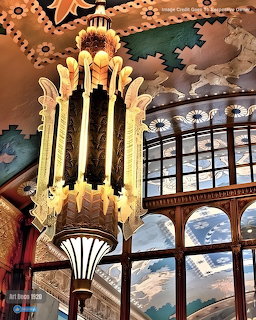 Golden Art Deco chandelier hanging in ornate theater with decorative painted ceiling