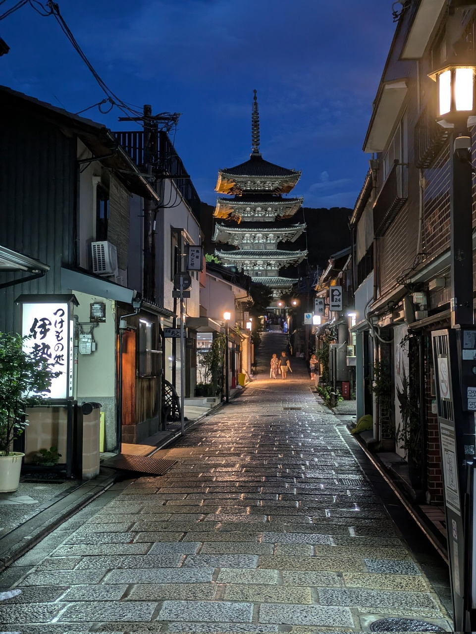 Narrow stone-paved street in Kyoto at night with lanterns and a five-story pagoda in the background
