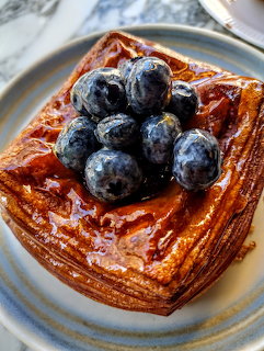Golden Danish pastry topped with fresh blueberries on a blue-rimmed plate