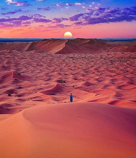 Person walking in desert sand dunes at sunset with purple sky