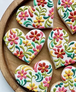 Heart-shaped cookies with vibrant floral icing designs on wooden plate