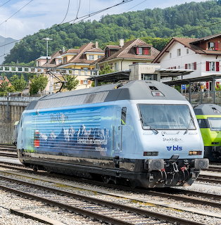 Silver and blue electric locomotive numbered 663 at train station with buildings and hills behind