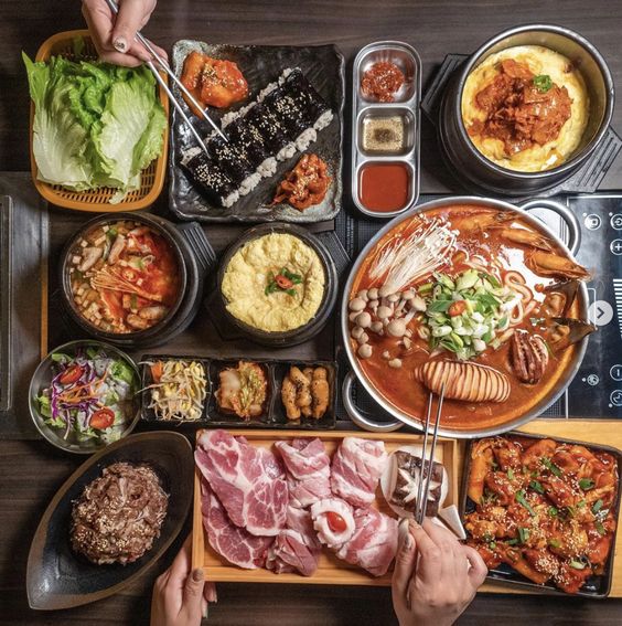 Overhead view of Korean BBQ with grilled meats, lettuce wraps, kimchi, and various side dishes on wooden table
