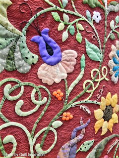Close-up of colorful floral applique on burgundy quilted fabric with embroidered flowers and vines