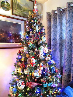 Decorated Christmas tree with multicolored ornaments and lights in a living room with framed pictures and curtains