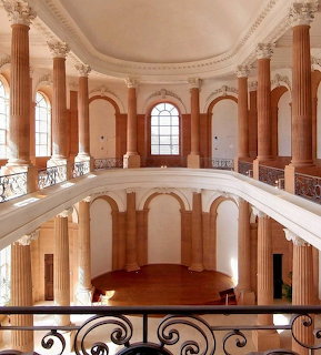 Two-story circular hall with pink marble columns, white balcony railings, and tall arched windows in classical style