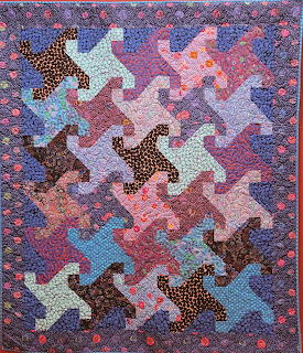 Colorful patchwork quilt with interlocking puzzle-like tessellated shapes in purple, pink, and blue tones
