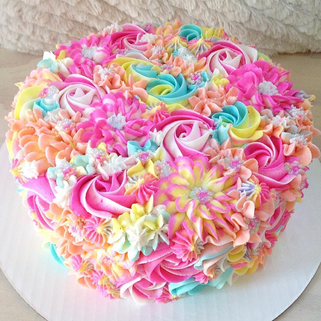 Round cake covered in rainbow-colored buttercream rosettes and piped flowers
