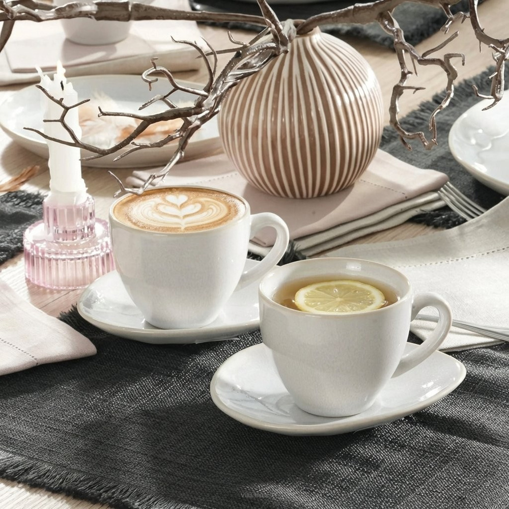 Two white cups of coffee and tea on saucers beside a vase and decorative branches